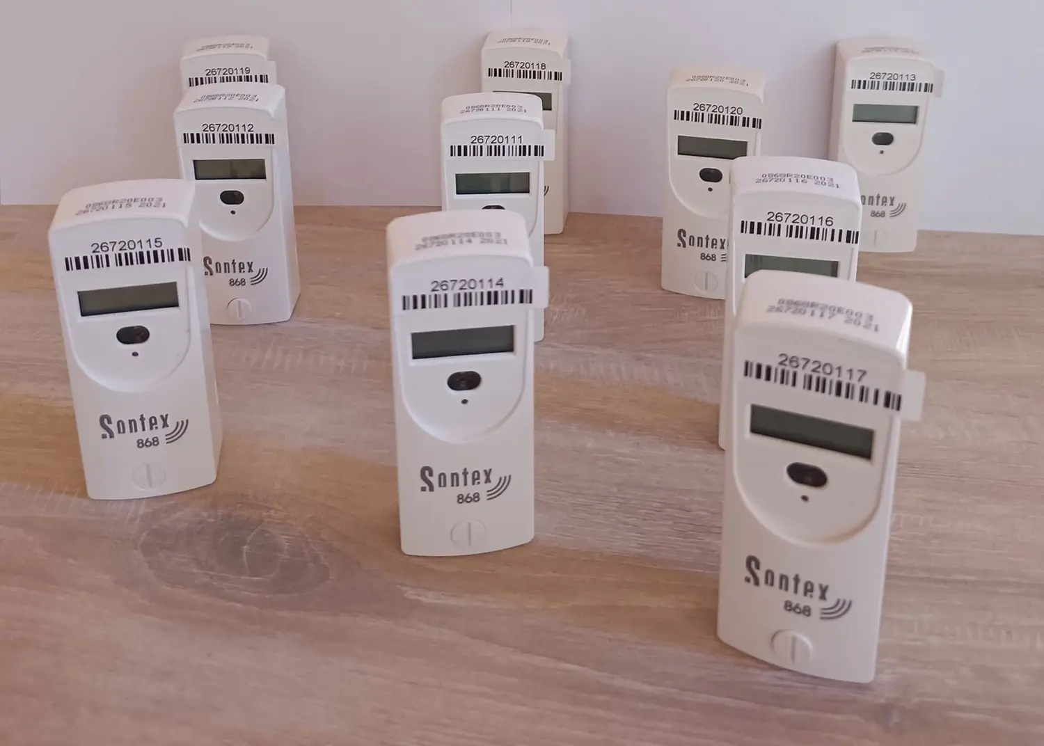 Fair Therm GmbH - Rechtskonforme Abrechnung und Analyse -Mehrere weiße, vertikale elektronische Geräte, wahrscheinlich Wärmekostenverteiler, mit digitalen Anzeigen und Barcodes, einige mit der Aufschrift „Sontex“ oder „Santex“.